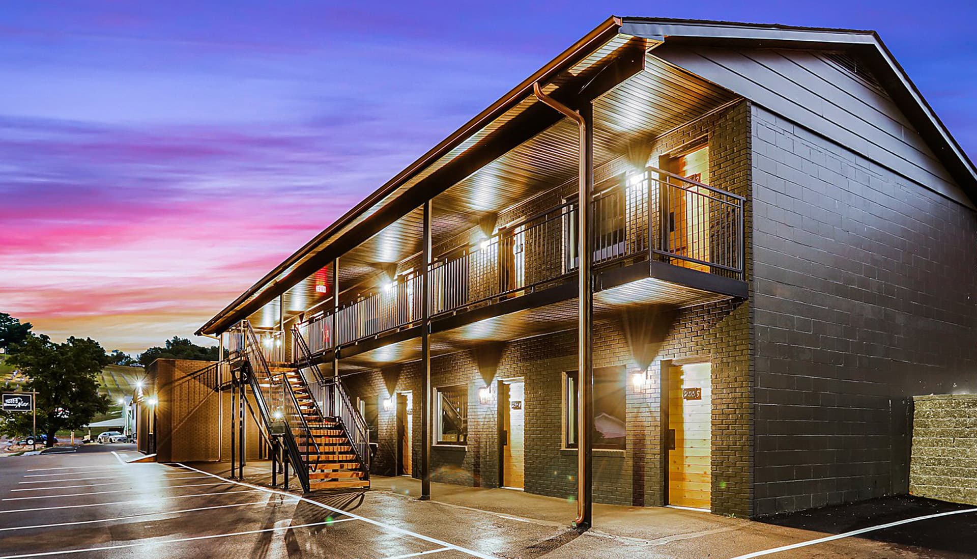 A modern two-story motel lit at dusk with a colorful sky in the background.