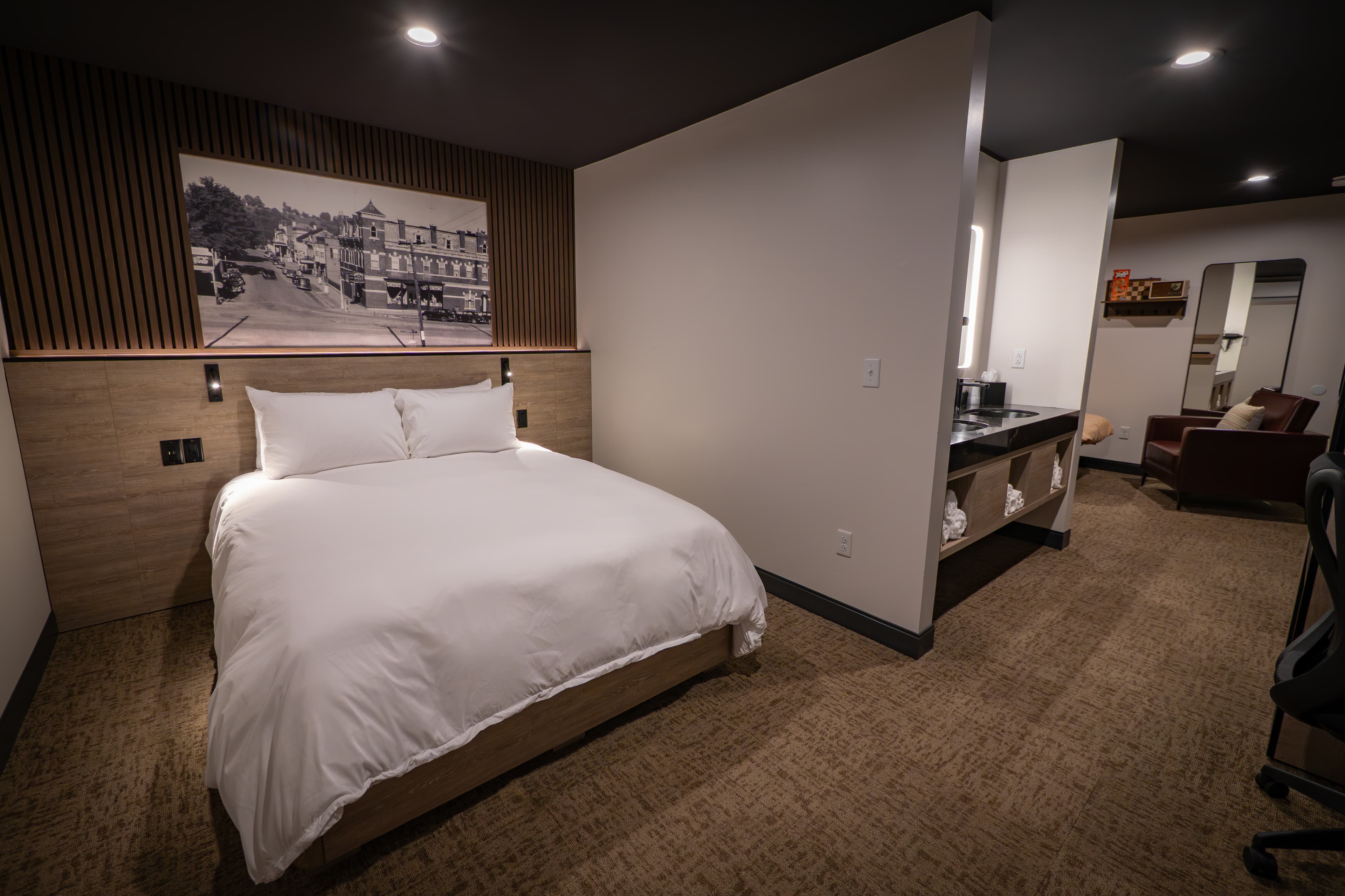 A modern hotel room featuring a queen bed, desk area, and a wall-mounted artwork.
